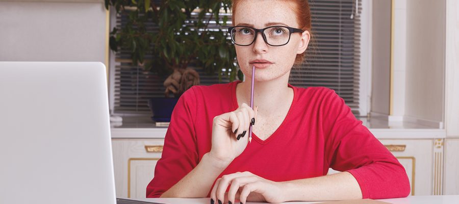 Thoughtful successful young female copywriter tries to get good ideas for new project, puts down notes in diary, works remotely on laptop computer, wants to creat something unsual and creative